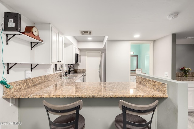 kitchen featuring stainless steel appliances, kitchen peninsula, light stone countertops, and white cabinets