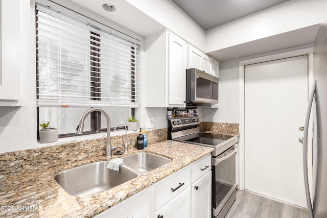 kitchen featuring appliances with stainless steel finishes, white cabinetry, sink, light stone counters, and light hardwood / wood-style flooring