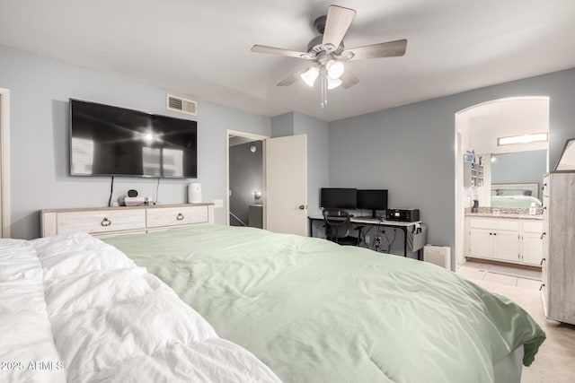 bedroom with connected bathroom, light colored carpet, and ceiling fan