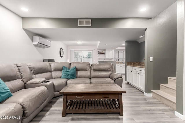 living room featuring sink, a wall unit AC, and light hardwood / wood-style flooring