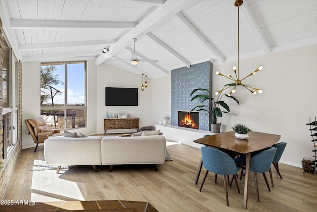 living room featuring ceiling fan, a large fireplace, lofted ceiling with beams, and light wood-type flooring