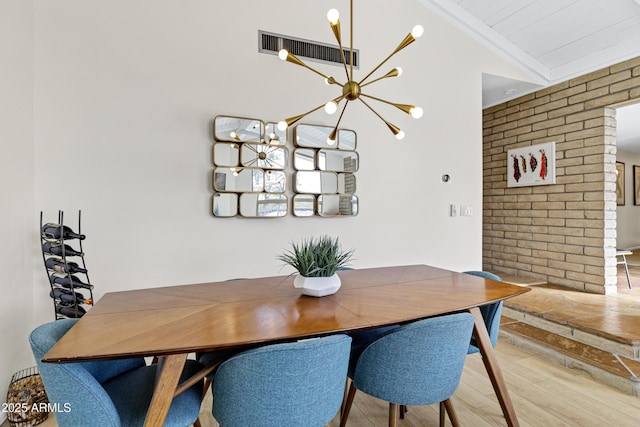 dining area featuring brick wall, wood-type flooring, a chandelier, and vaulted ceiling