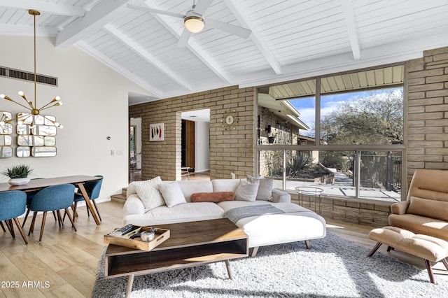 living room featuring vaulted ceiling with beams, ceiling fan with notable chandelier, light hardwood / wood-style flooring, and brick wall