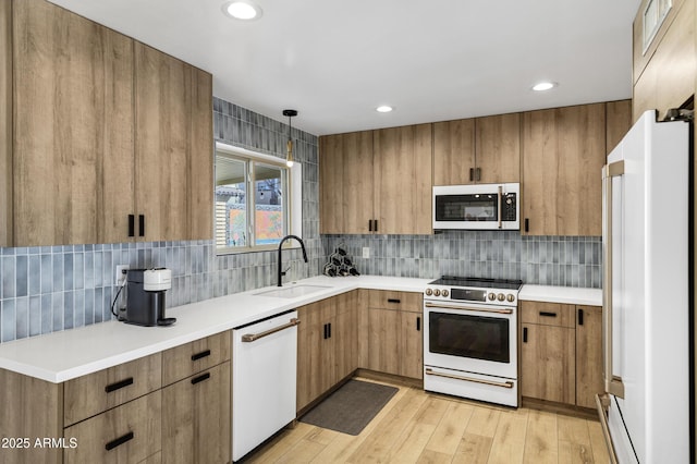 kitchen with sink, white appliances, light hardwood / wood-style flooring, hanging light fixtures, and backsplash