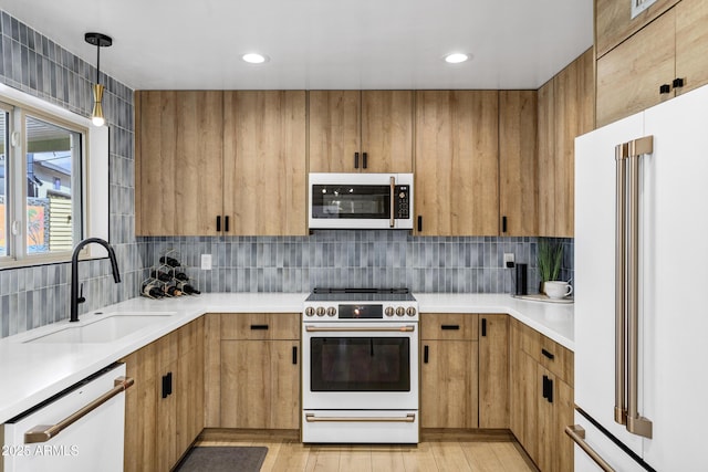 kitchen featuring sink, white appliances, light hardwood / wood-style flooring, hanging light fixtures, and tasteful backsplash