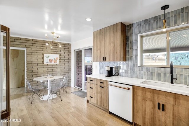 kitchen with tasteful backsplash, sink, hanging light fixtures, white dishwasher, and light hardwood / wood-style floors