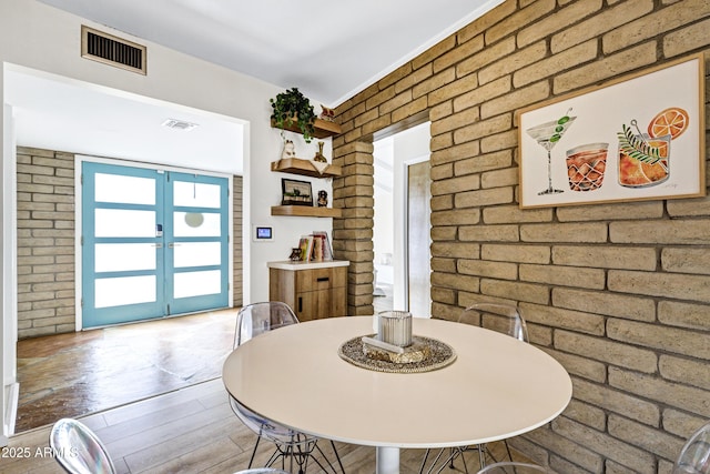 dining space featuring hardwood / wood-style flooring, brick wall, and french doors