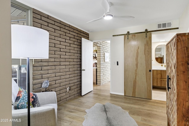 living area featuring ceiling fan, brick wall, a barn door, and light hardwood / wood-style floors