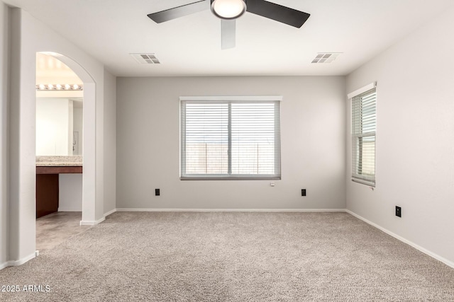 unfurnished bedroom featuring ceiling fan, arched walkways, visible vents, and light carpet