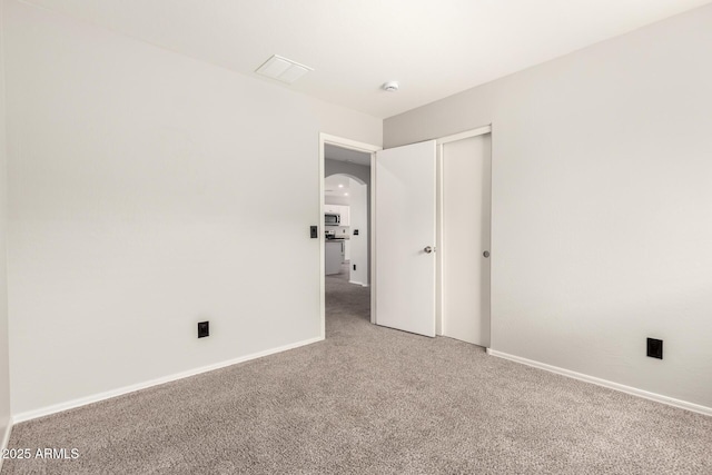 unfurnished bedroom featuring baseboards, arched walkways, a closet, and carpet flooring