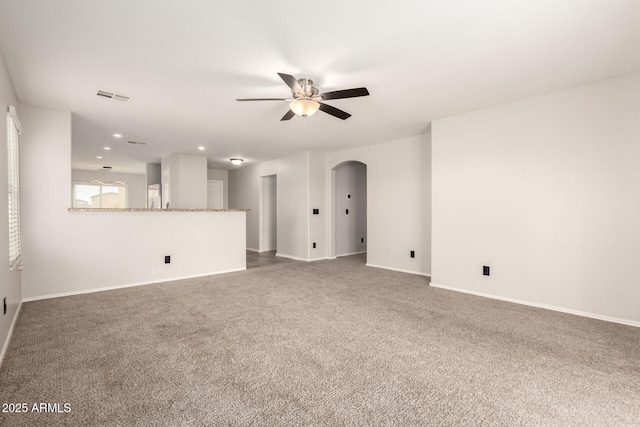 unfurnished living room featuring visible vents, a ceiling fan, arched walkways, carpet floors, and baseboards