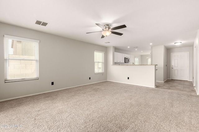 unfurnished living room with a ceiling fan, light colored carpet, visible vents, and baseboards