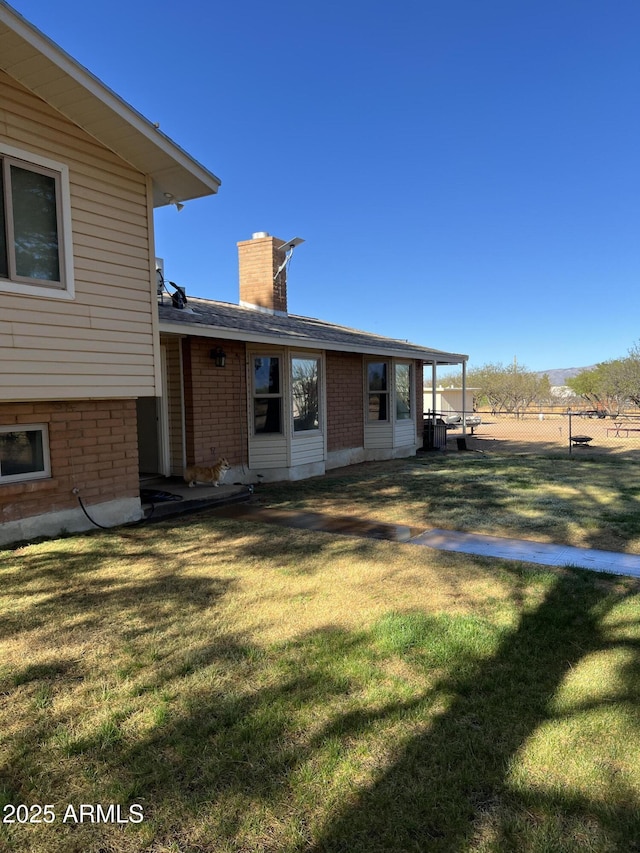 rear view of property with brick siding, fence, a yard, and a chimney