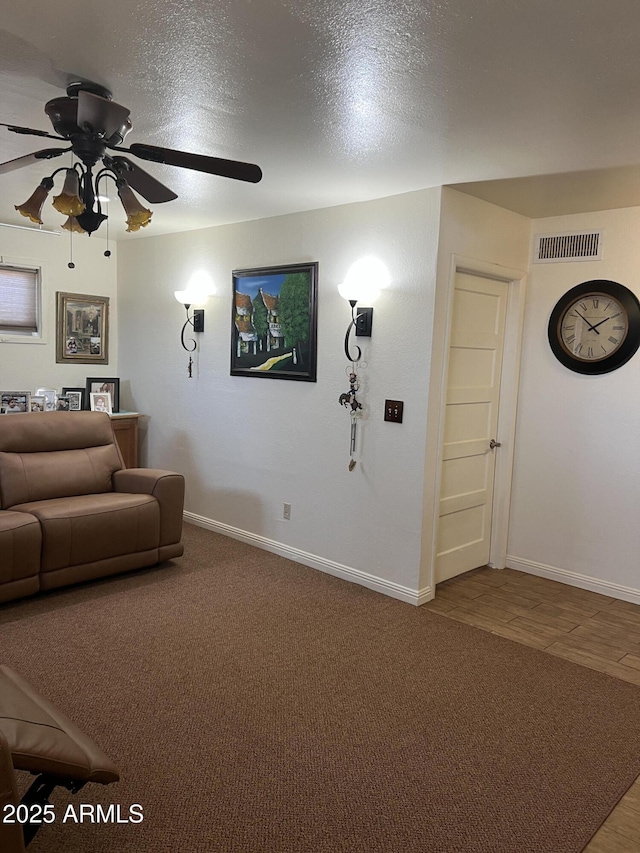 living area featuring visible vents, carpet floors, baseboards, a textured ceiling, and a ceiling fan
