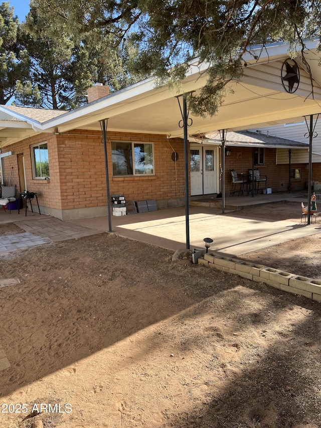 back of property featuring brick siding, a patio area, a chimney, and a carport