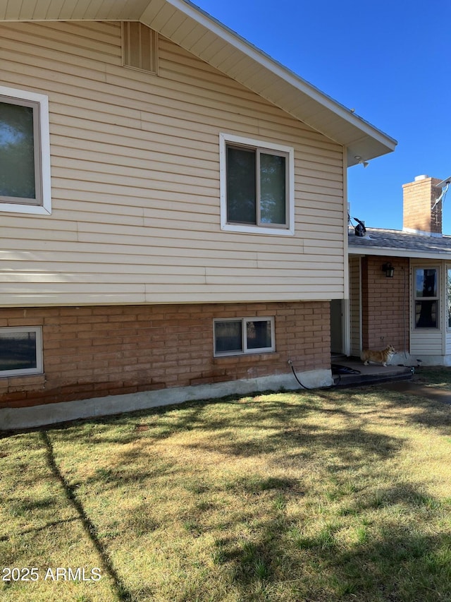 view of side of home featuring a lawn, brick siding, and a chimney