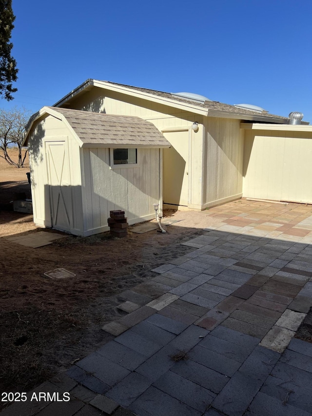 rear view of house with a storage shed, a patio, an outbuilding, and roof with shingles
