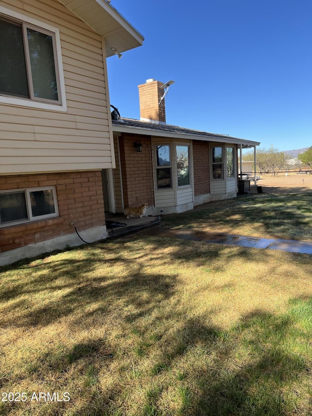 back of house featuring a chimney, a yard, and brick siding