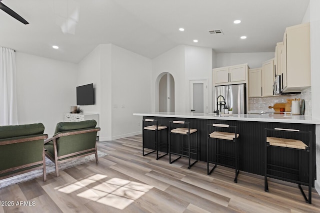 kitchen featuring kitchen peninsula, light hardwood / wood-style flooring, stainless steel appliances, a kitchen bar, and backsplash