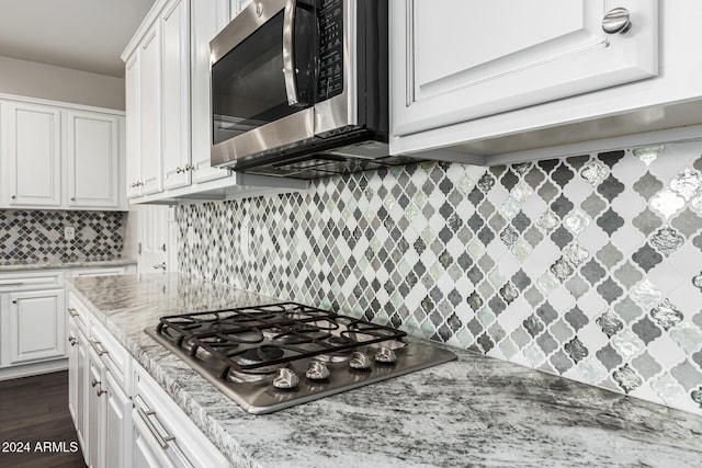 kitchen featuring stainless steel appliances, white cabinetry, tasteful backsplash, light stone countertops, and dark wood-style flooring