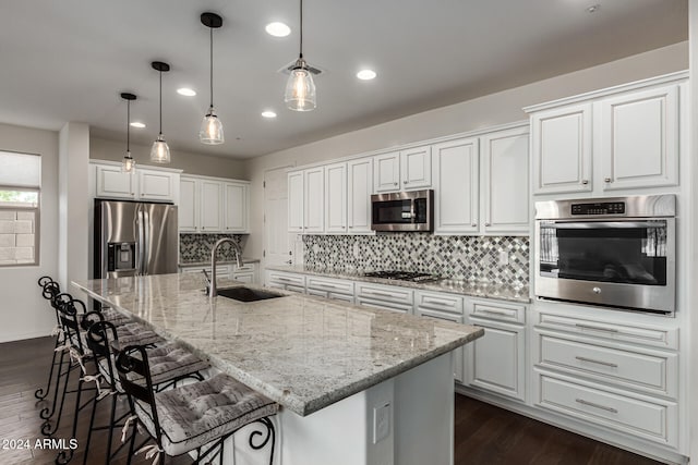 kitchen featuring stainless steel appliances, sink, pendant lighting, white cabinets, and an island with sink