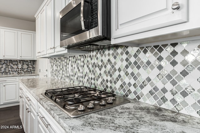 kitchen featuring light stone countertops, stainless steel appliances, dark hardwood / wood-style flooring, decorative backsplash, and white cabinets