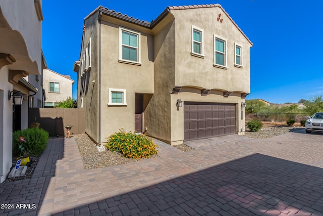 view of front of property with an attached garage, stucco siding, fence, and decorative driveway