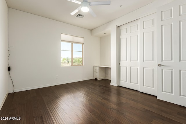 unfurnished bedroom featuring ceiling fan, a closet, built in desk, and dark wood-type flooring