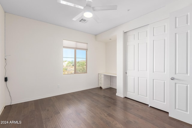 unfurnished bedroom with built in desk, a closet, dark wood-type flooring, and ceiling fan