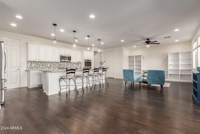 kitchen featuring appliances with stainless steel finishes, a center island with sink, dark hardwood / wood-style floors, white cabinetry, and hanging light fixtures