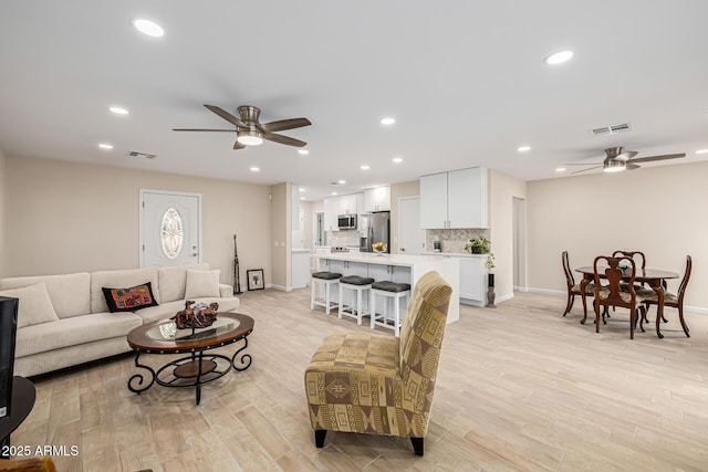 living room with light wood finished floors, visible vents, and ceiling fan