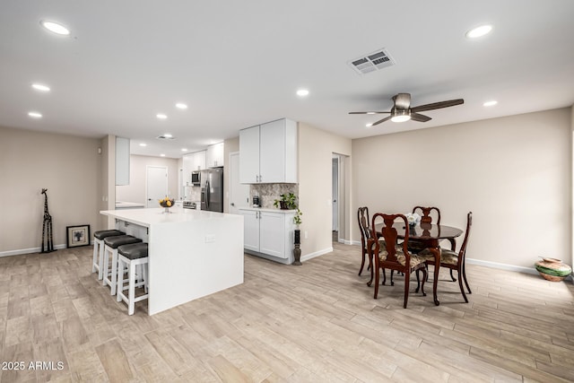 kitchen featuring visible vents, backsplash, a kitchen island, stainless steel fridge, and white cabinets