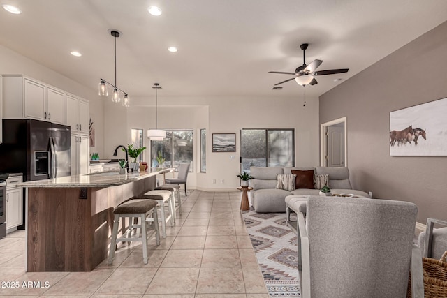 kitchen with light stone countertops, a kitchen breakfast bar, decorative light fixtures, a kitchen island with sink, and white cabinets