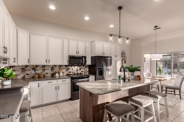 kitchen featuring a kitchen bar, appliances with stainless steel finishes, a kitchen island with sink, white cabinetry, and hanging light fixtures