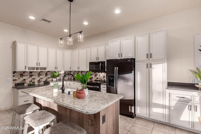 kitchen featuring a kitchen bar, appliances with stainless steel finishes, a kitchen island with sink, white cabinets, and hanging light fixtures