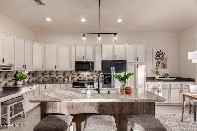 kitchen featuring a kitchen island with sink, light stone counters, decorative light fixtures, and appliances with stainless steel finishes