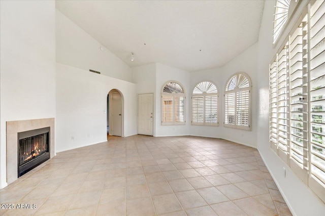 unfurnished living room featuring light tile patterned floors, a tile fireplace, and high vaulted ceiling