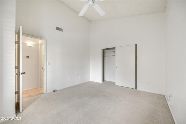 unfurnished bedroom featuring a towering ceiling, light carpet, ceiling fan, and a closet