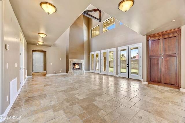 unfurnished living room featuring french doors, a towering ceiling, and a tiled fireplace