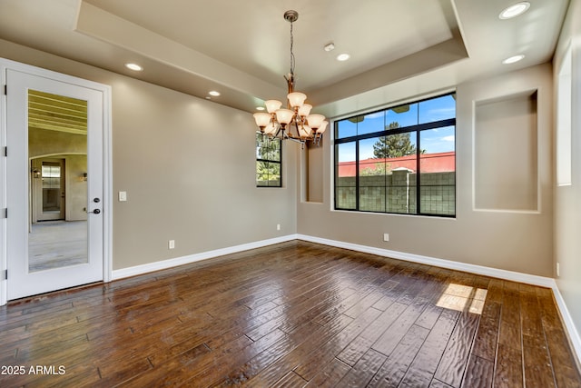 spare room with dark hardwood / wood-style floors, an inviting chandelier, and a tray ceiling