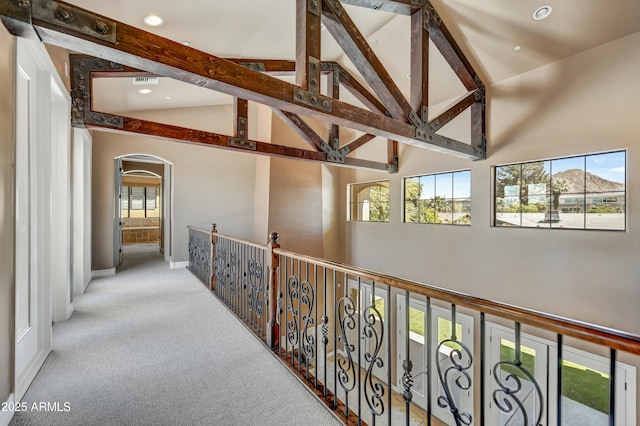 corridor with light colored carpet, beam ceiling, and high vaulted ceiling