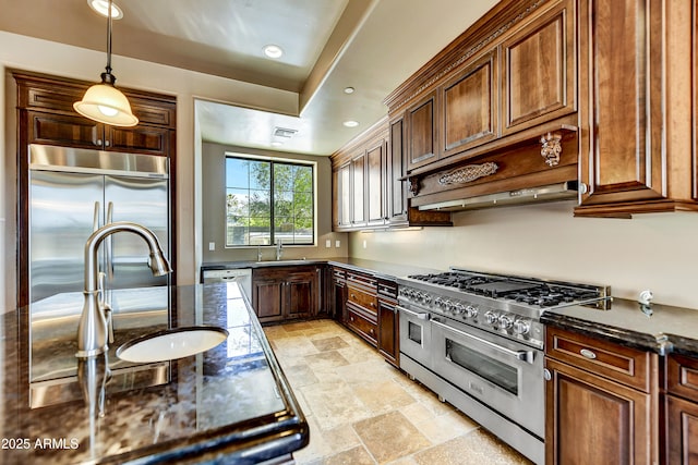 kitchen with appliances with stainless steel finishes, decorative light fixtures, sink, dark stone countertops, and custom range hood