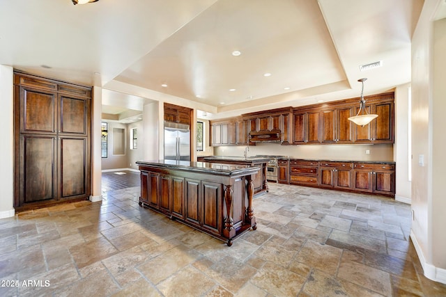 kitchen featuring stainless steel built in refrigerator, decorative light fixtures, and a center island with sink