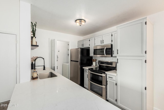 kitchen with washing machine and dryer, a sink, white cabinetry, light countertops, and appliances with stainless steel finishes