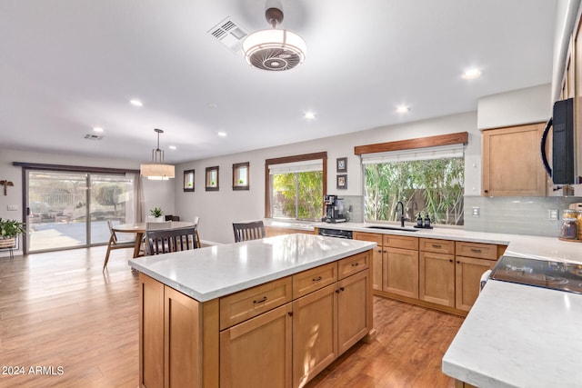 kitchen with light wood-type flooring, tasteful backsplash, decorative light fixtures, a center island, and sink