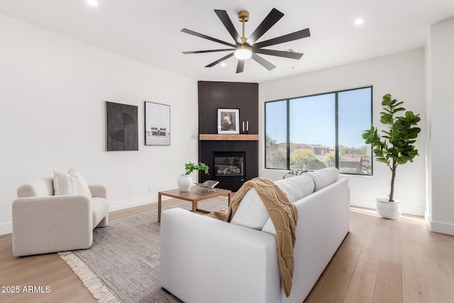 living room with ceiling fan, a large fireplace, and light hardwood / wood-style floors