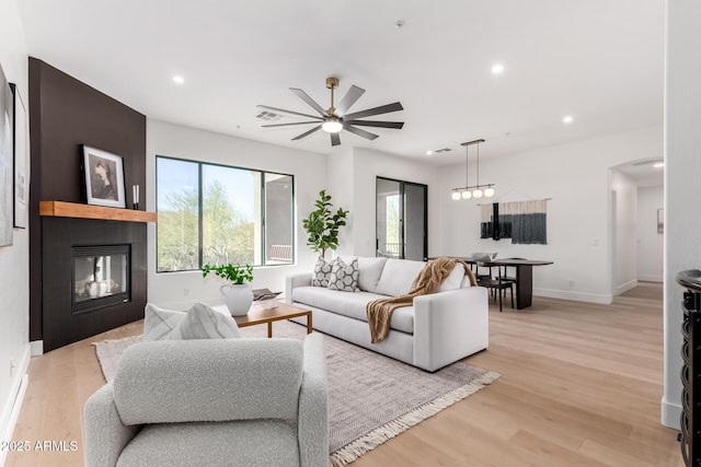 living room with ceiling fan, a multi sided fireplace, a wealth of natural light, and light wood-type flooring