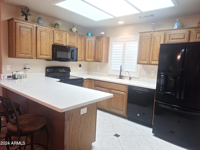 kitchen featuring sink, kitchen peninsula, a breakfast bar, light tile patterned floors, and black appliances