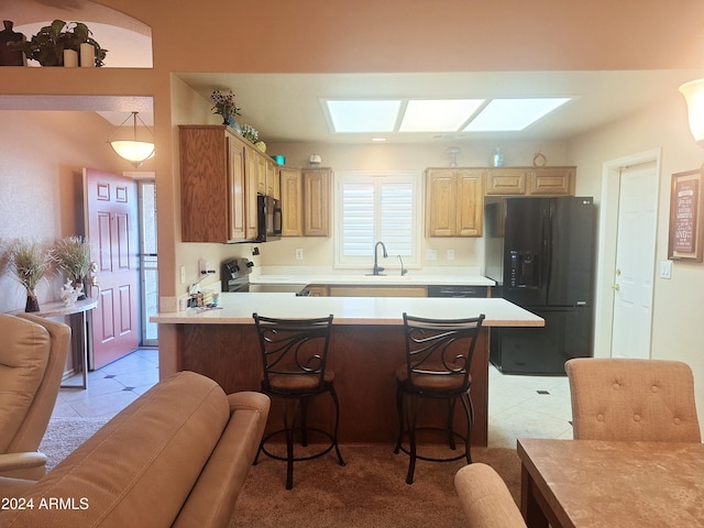 kitchen with a skylight, refrigerator with ice dispenser, light tile patterned flooring, a kitchen bar, and range