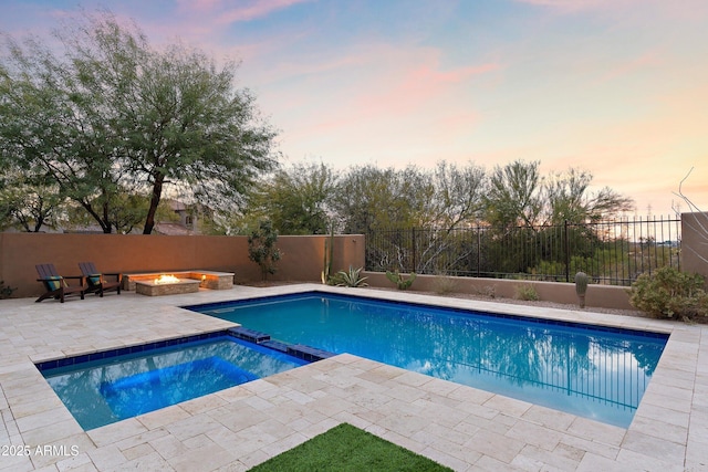 pool at dusk featuring a fire pit, a patio area, and an in ground hot tub